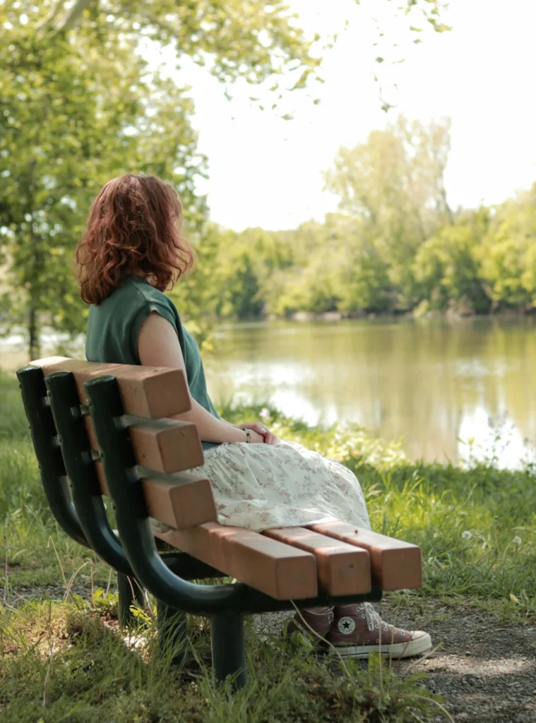 Woman sitting quietly on a bench by the lake, symbolizing reflection and uncertainty during midlife transition.