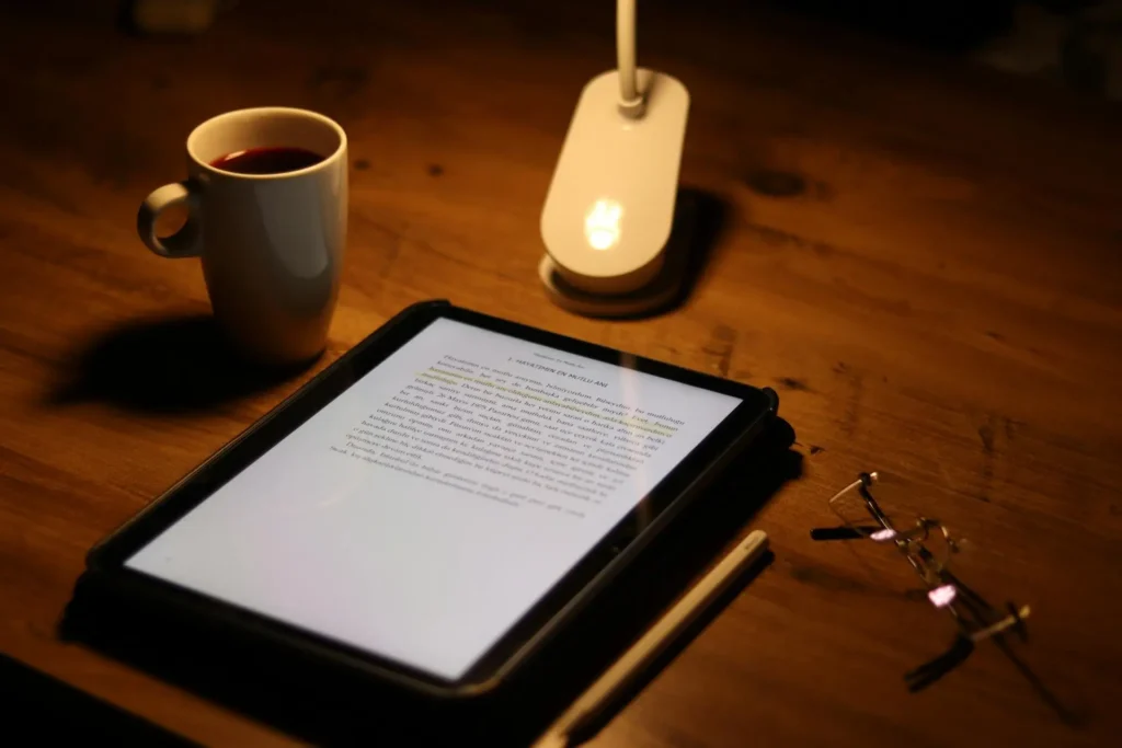 Warmly lit desk with a journal, tablet, coffee cup, and reading glasses, representing quiet reflection and intentional slowing down.