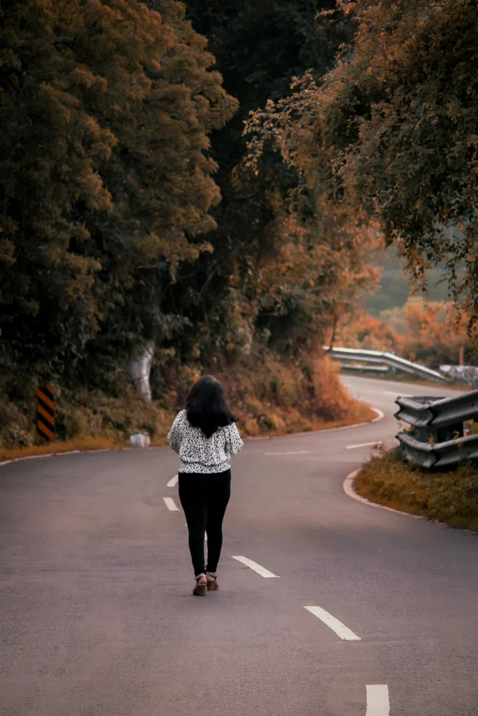 Woman walking alone along a quiet forest road, symbolizing self-reflection, emotional transition, and the midlife journey.